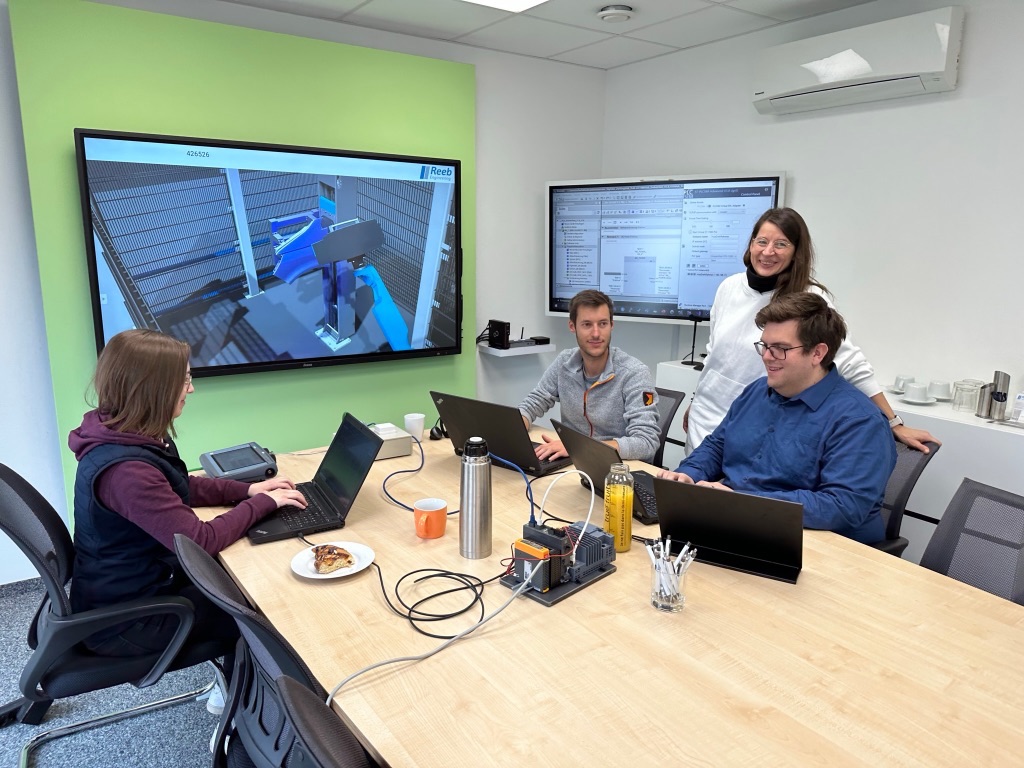 Vier Mitarbeiter sitzen an ihren Laptops im Konferenzraum in einer Besprechung